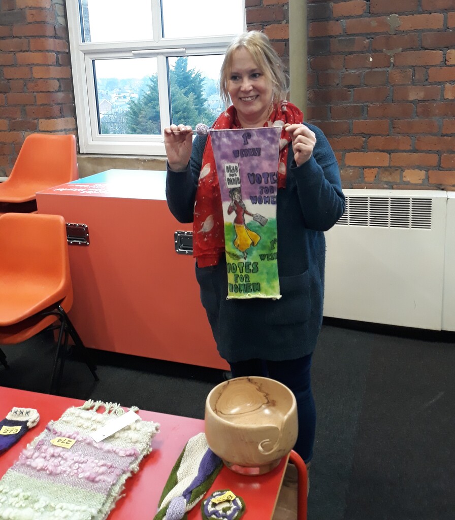 Julie holding a sock blank painted with a Votes for Women theme