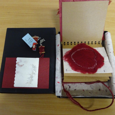 Felted and crochet heart, in red. Part of a ring-bound book, in an open box.