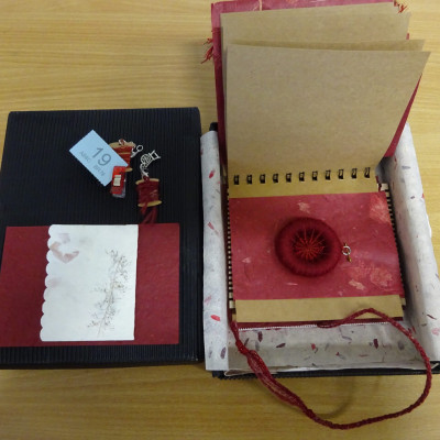 Dorset button, in red. Part of a ring-bound book, in an open box.
