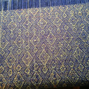Close up of some fabric being woven on a loom. Blue and gold colours.